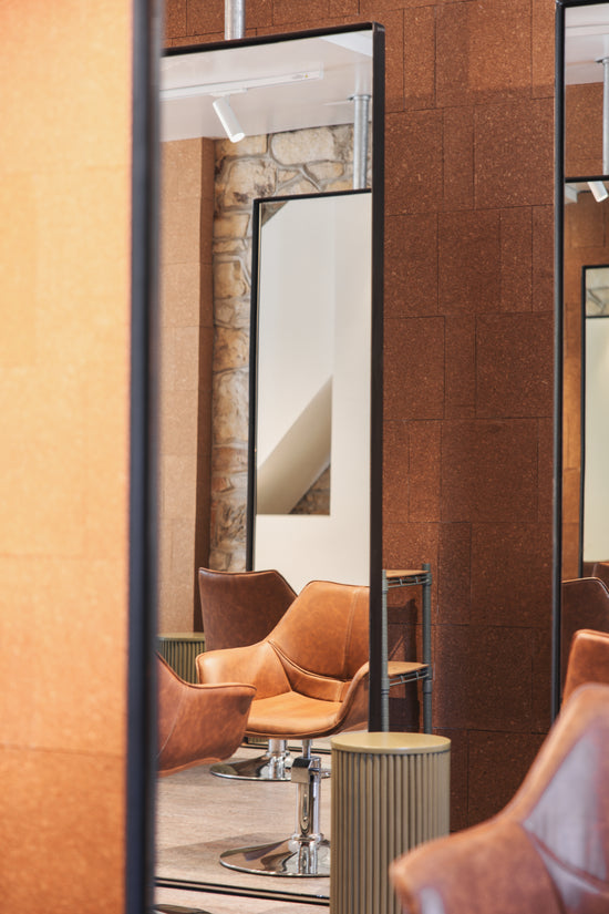 A reflection in the mirror capturing **Neighbourhood Salon's** inviting interior—**corkboard walls**, **sandstone leather chairs**, and an **olive side table**—blending warm textures and earthy tones for a stylish and welcoming space in **Darlinghurst, Sydney, near Surry Hills**.