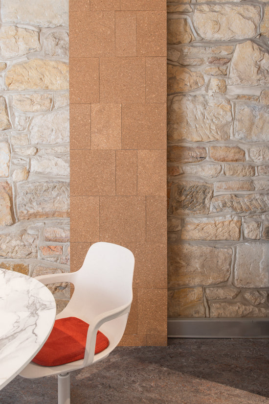 A stylish corner of **Neighbourhood Salon** in **Darlinghurst, Sydney, near Surry Hills**, featuring a **corkboard and sandstone wall**, a sleek **white marble table**, and a **white chair with an orange-red cushion**, creating a warm and modern aesthetic.