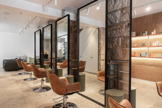 The interiors of Neighbourhood Salon, Darlinghurst feature warm sandstone walls, sleek mirrors, and plush brown leather chairs, complemented by minimalist decor and soft lighting—creating a welcoming and luxurious atmosphere.